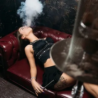 Woman exhaling hookah smoke on a leather sofa, beginner guide to smoking hookah