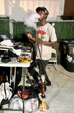 Guest smoking hookah at an outdoor event next to the hookah maker's service station